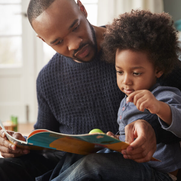 Father And Young Son Reading Book Together At Home